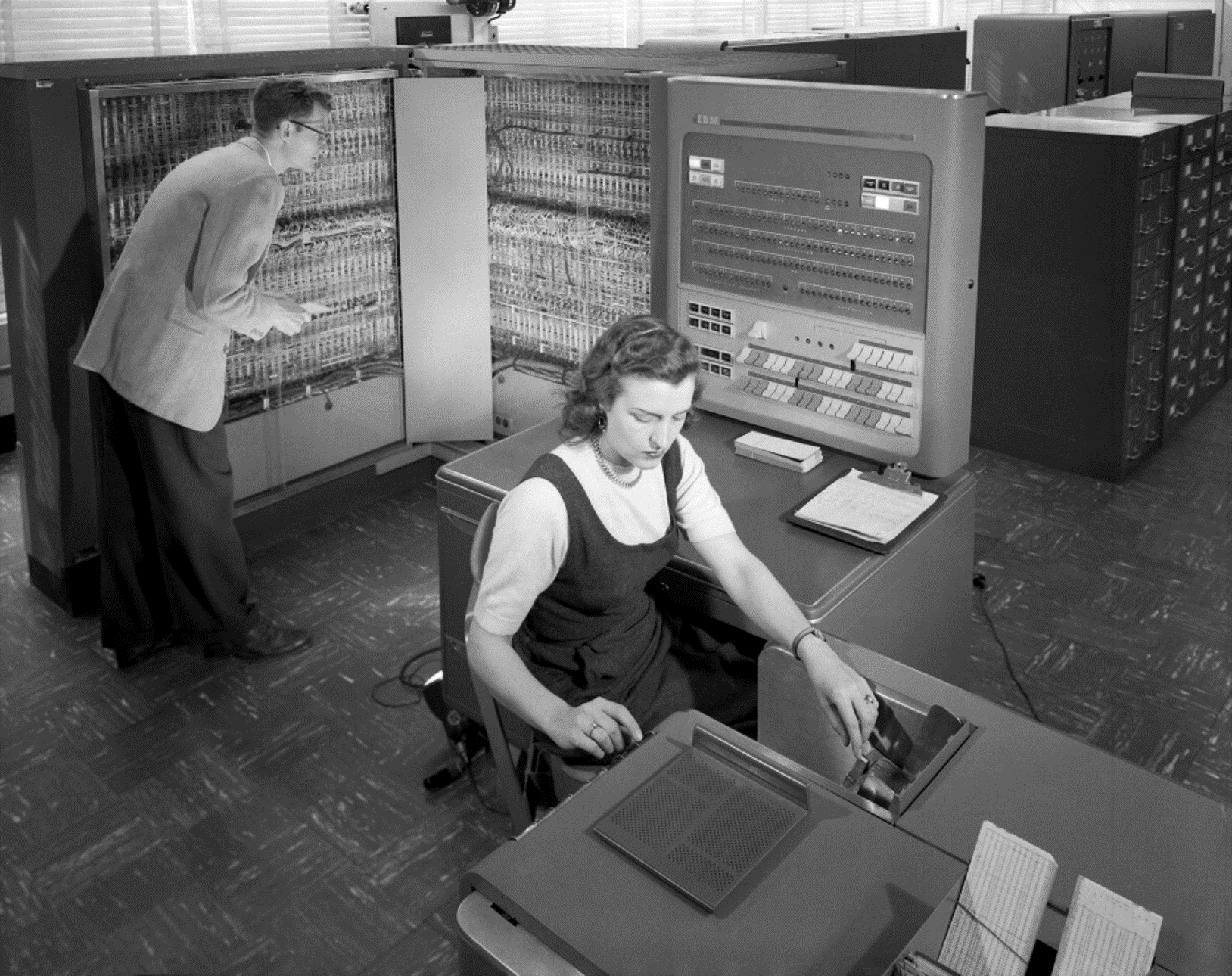 Man and woman shown working with IBM type 704 electronic data processing machine used for making computations for aeronautical research at Langley Research Center.